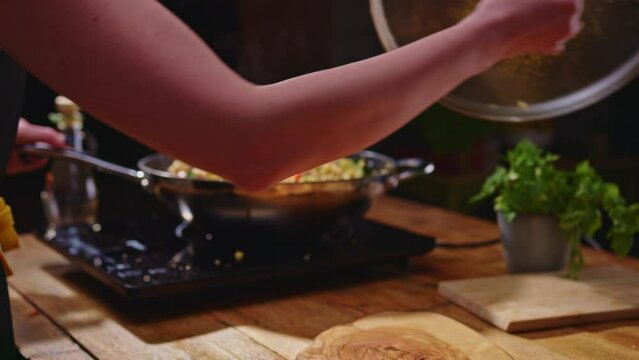 Woman cooking frying meat and vegetables in wok pan on kitchen table. Closeup hands. Real, authentic cooking.