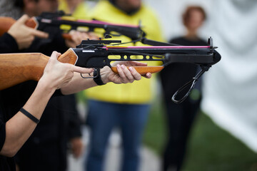 girl shoots from a crossbow close-up. A young girl is aiming at a target with a crossbow. girl shoots from a crossbow in a summer outdoor shooting range.