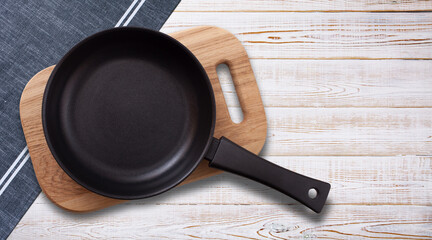 Black fry pan and board with napkin on wooden table. Top view mockup - obrazy, fototapety, plakaty