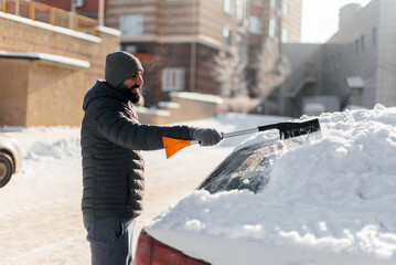 A young man cleans his car after a snowfall on a sunny, frosty day. Cleaning and clearing the car...