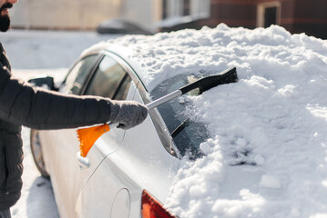 A young man cleans his car after a snowfall on a sunny, frosty day. Cleaning and clearing the car...