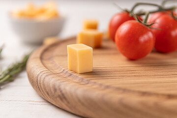 round wooden cutting board with edging. cherry tomatoes, slices of cheese and spices on a white background. mockup with copy space for text, side view, close-up