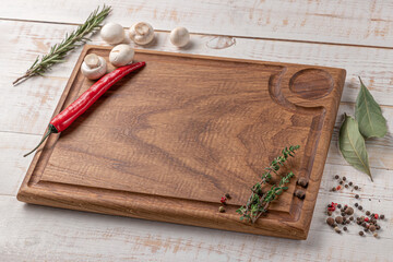 square wooden cutting board of dark color with edging. mushrooms, chili pepper and spices on a...