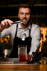 Great close-up on ice cube over glass with cocktail on bar counter