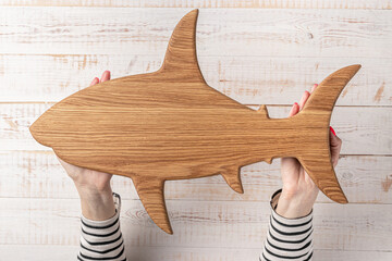 hands of a woman holdind a wooden cutting board shaped fish or shark above a white background....