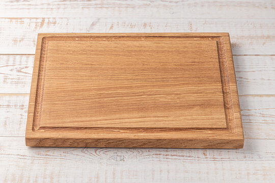 rectangular cutting board with edging on a white wooden table. mockup of a food background with copy space, side view