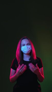 Online instruction. Quarantine measures. Happy woman in medicine mask informing about pandemic protection looking at camera isolated on black neon light vertical. Virtual communication. New normal