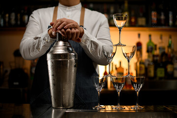 Close-up view of large shaker and pyramid of empty glasses stands on bar