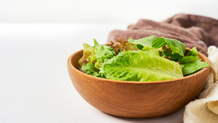 fresh salad from green leaves in a wooden bowl on white clean mood background with copy space                                                  