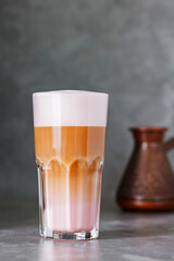 Latte macchiato coffee on a gray background. Hot latte macchiato with rose milk in transparent glass. Close up