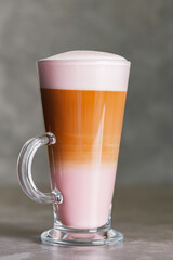 Latte macchiato coffee on a gray background. Hot latte macchiato with rose milk in transparent glass. Close up