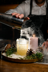 close-up view of crystal glass with ice cubes in which pour a steaming drink from a steel shaker.
