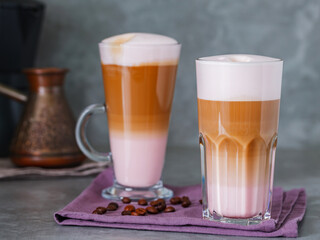 Two glasses of latte macchiato and roasted coffee beans on a linen napkin. Latte macchiato coffee and coffee makers on gray background