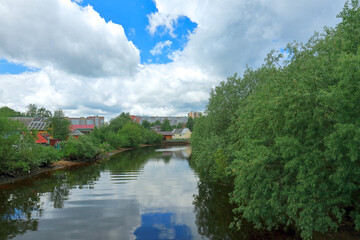Beautiful summer view of the river in the city with overgrown banks. Russia, Arkhangelsk, Solombalka River