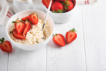 Cottage cheese with strawberries. Breakfast from cottage cheese with slices fresh strawberries, cream, cup of coffee in white bowl on white wooden background. Top view. Food concept. Mock up.