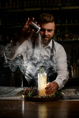 professional male bartender decorates glass with a steaming cocktail on the bar counter