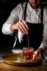 hand of bartender mixes a cocktail in glass with spoon