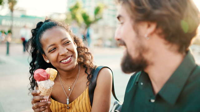 Closeup portrait of happy interracial couple eating ice cream in urban city background. Close-up of a man and woman tasting ice cream. Backlight