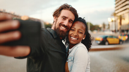 Closeup of smiling interracial couple taking a selfie on fountain background. Close-up, man and woman video chatting using a mobile phone