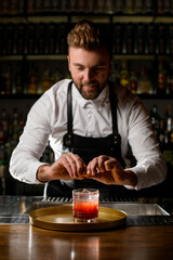 Man bartender gently sprinkles by citrus peel on glass with cocktail