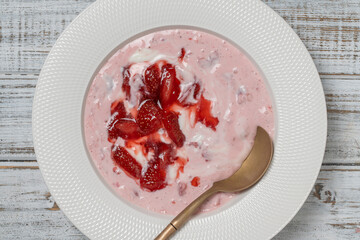 White plate with red strawberries and natural yogurt on a wooden table, top view