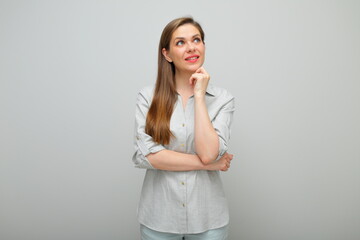 Smiling thinking woman with her chin on hand looking up, isolated female portrait, young lady dressed pants and gray shirt.