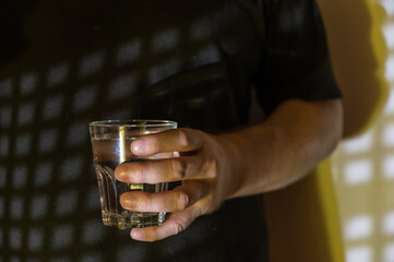 Middle plan of a mature man holding a glass of water in his hand. A repeating geometric pattern of square patches of light. Abstract pattern of light and shadow. Selective focus. Low key.