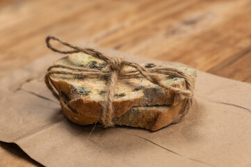 Moldy bread against a wooden background. Two slices of wheat bread covered in fungal mold. The slices are tied with twine. Brown paper bag. Spoiled food. Selective focus.