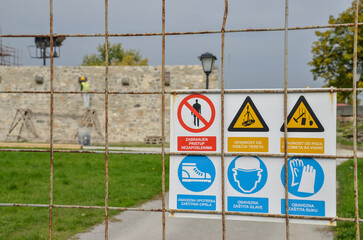 Safety and warning signs at construction site. Symbols on wired fence near building under construction.  