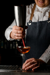 bartender masterfully decorates glass of cocktail with whipped cream on the bar counter