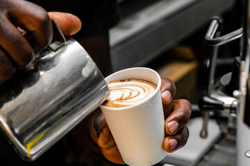 African Coffee Barista pouring a heart shape with milk foam.