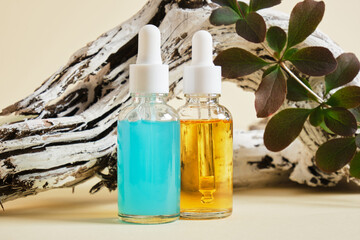 blue and orange serums in transparent dropper bottles on the background of a wooden snag and a branch