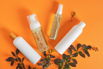 everal mock up cosmetic bottles and branch with leaves and flowers on orange background copy space...