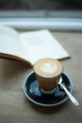 Coffee Cortado (piccolo latte) in a glass on a plate, with opened book behind