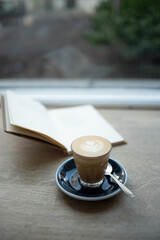Coffee Cortado (piccolo latte) in a glass on a plate, with opened book behind