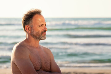 Fototapeta na wymiar Portrait of a bearded shirtless middle aged man in profile on the sea background in summer sunset