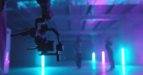 Back view of cameraman shooting video of dancers with electornic steadicam. Colorful neon light background. Slow motion. Backstage