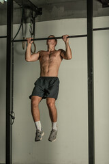 Fototapeta na wymiar Handsome bodybuilder doing pull-ups on horizontal bar in a indoors modern gym.