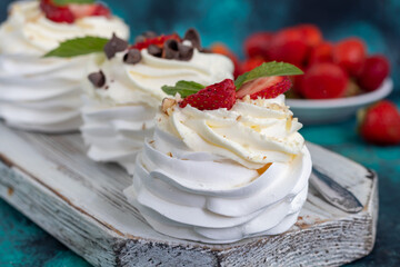 Pavlova meringue cakes with whipped cream and fresh strawberries, mint leaves. Selective focus.