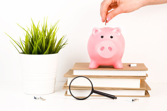 Hand putting money into piggy bank on top of books. Caot or savings for education