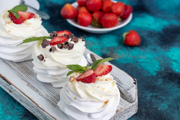 Pavlova meringue cakes with whipped cream and fresh strawberries, mint leaves. Selective focus.
