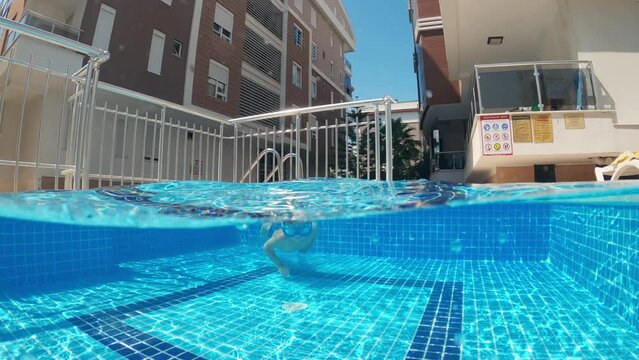 Child enjoying summer vacation. Underwater view of happy fun loving boy diving into swimming pool in summer sunny day. Slow motion.