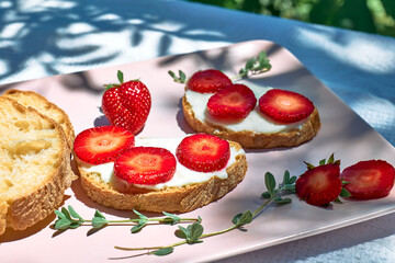 Summer delicious strawberry sandwich. Toast bread with spread stracchino cheese and slices of ripe red strawberry on pink plate on the table in the garden. Healthy eating, fruit dieting brunch.