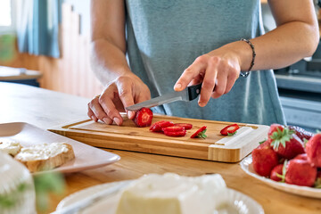 Obraz na płótnie Canvas Woman making summer strawberry sandwich. Female hands cutting ripe red strawberry on cutting board. Healthy eating, fruit dieting brunch.