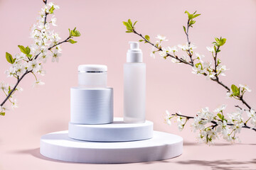 bottles for cosmetics on a round podium and branches of plum blossoms on a pink background
