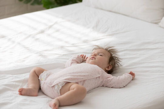 Close up shot peaceful babygirl in bodysuit and diaper falling asleep alone in bedroom, lying on bed looking carefree deep in sweet dreams. Daytime nap, healthy sleep for baby growth, babyhood concept