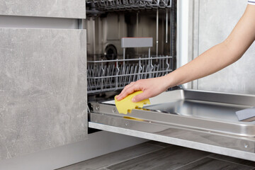 Woman hands cleaning dishwasher panel with yellow rag in kitchen. Close up.