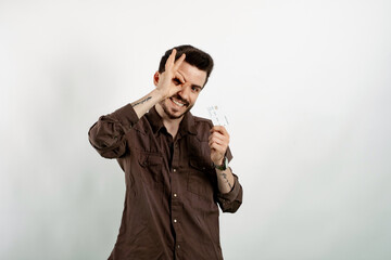 Fototapeta premium Happy young man wearing shirt posing isolated over white background holding credit bank card and showing okay gesture looking at the camera.