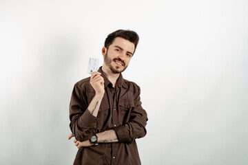 Young man smiling confident wearing casual clothes posing isolated over white background holding plastic credit or debit card while looking at the camera.