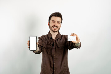 Cheerful young man wearing brown shirt posing isolated over white background holding credit or...